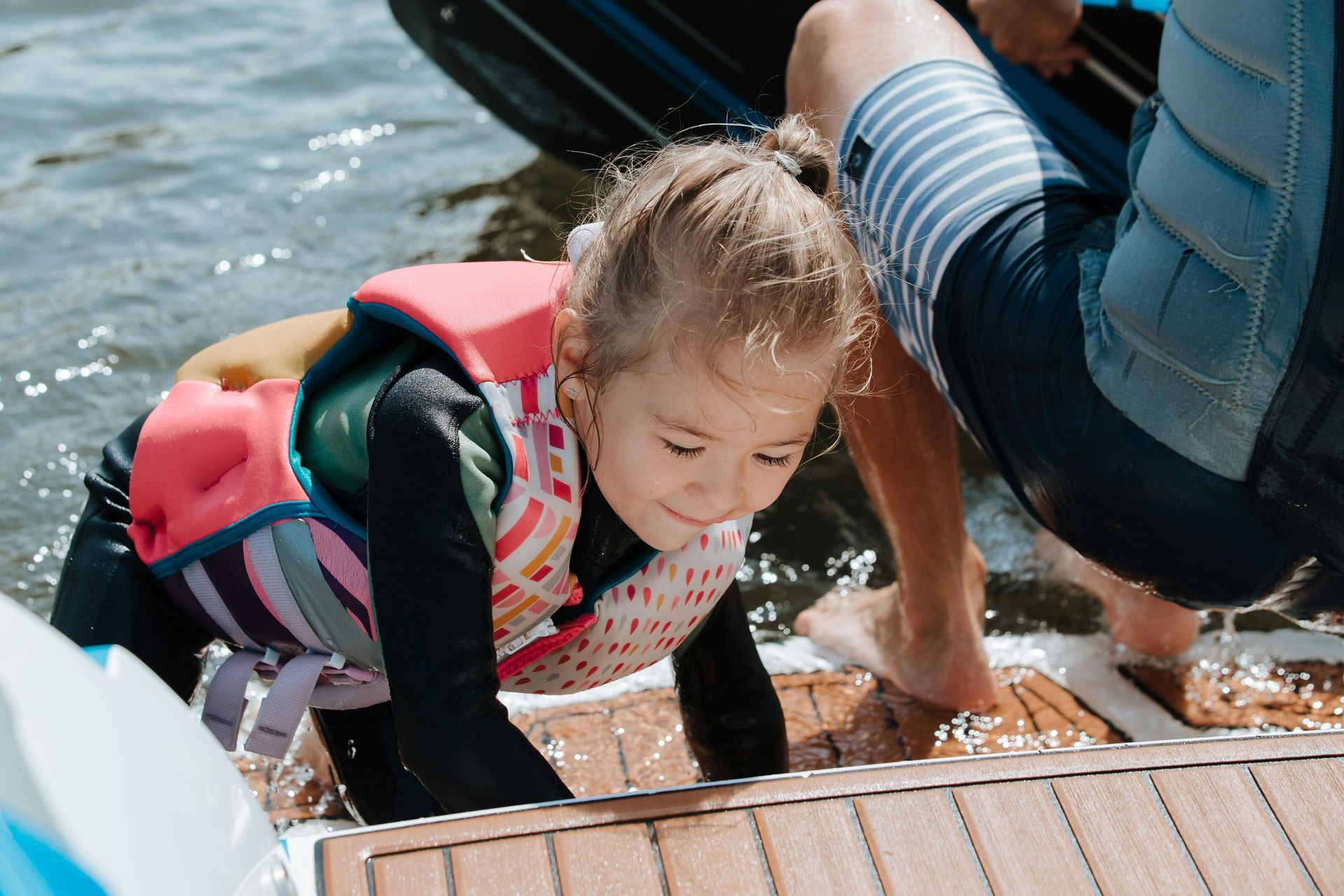 A little girl wearing a life jacket is crawling on the deck of a boat.