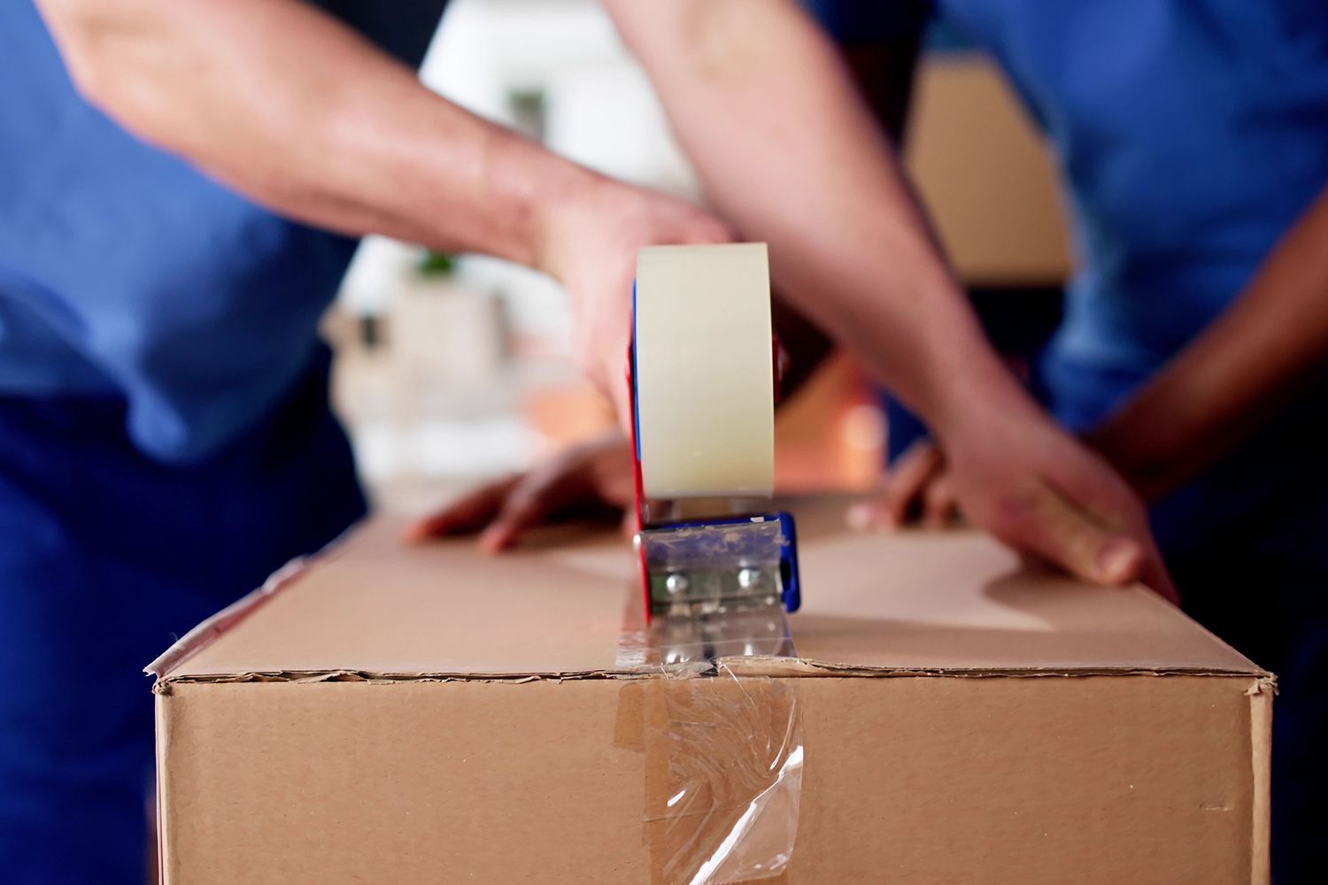 Specialists are closing a cardboard box with tape, showcasing commercial packaging supplies.