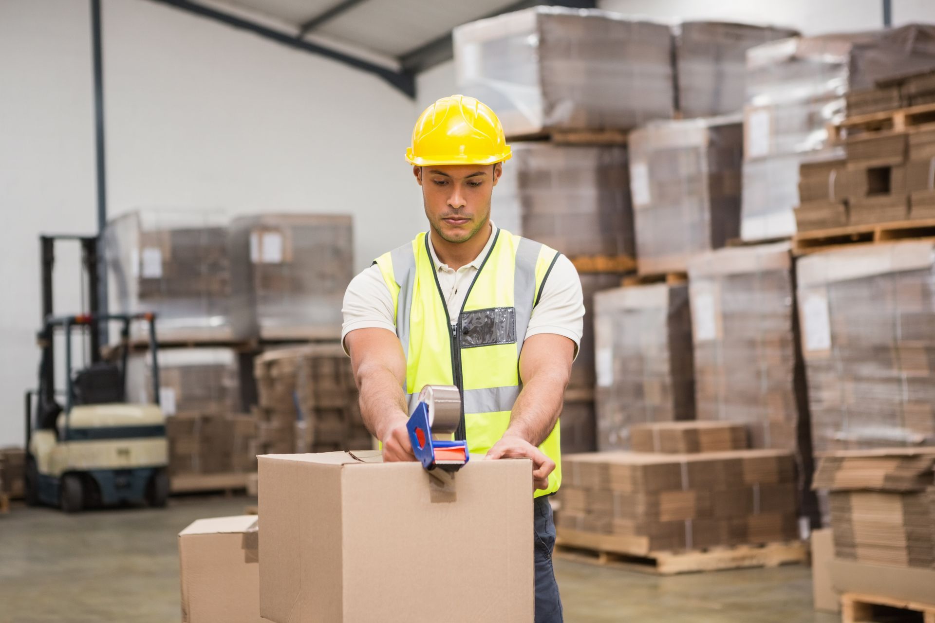 A warehouse labourer preparing a shipment by taping a cardboard box.