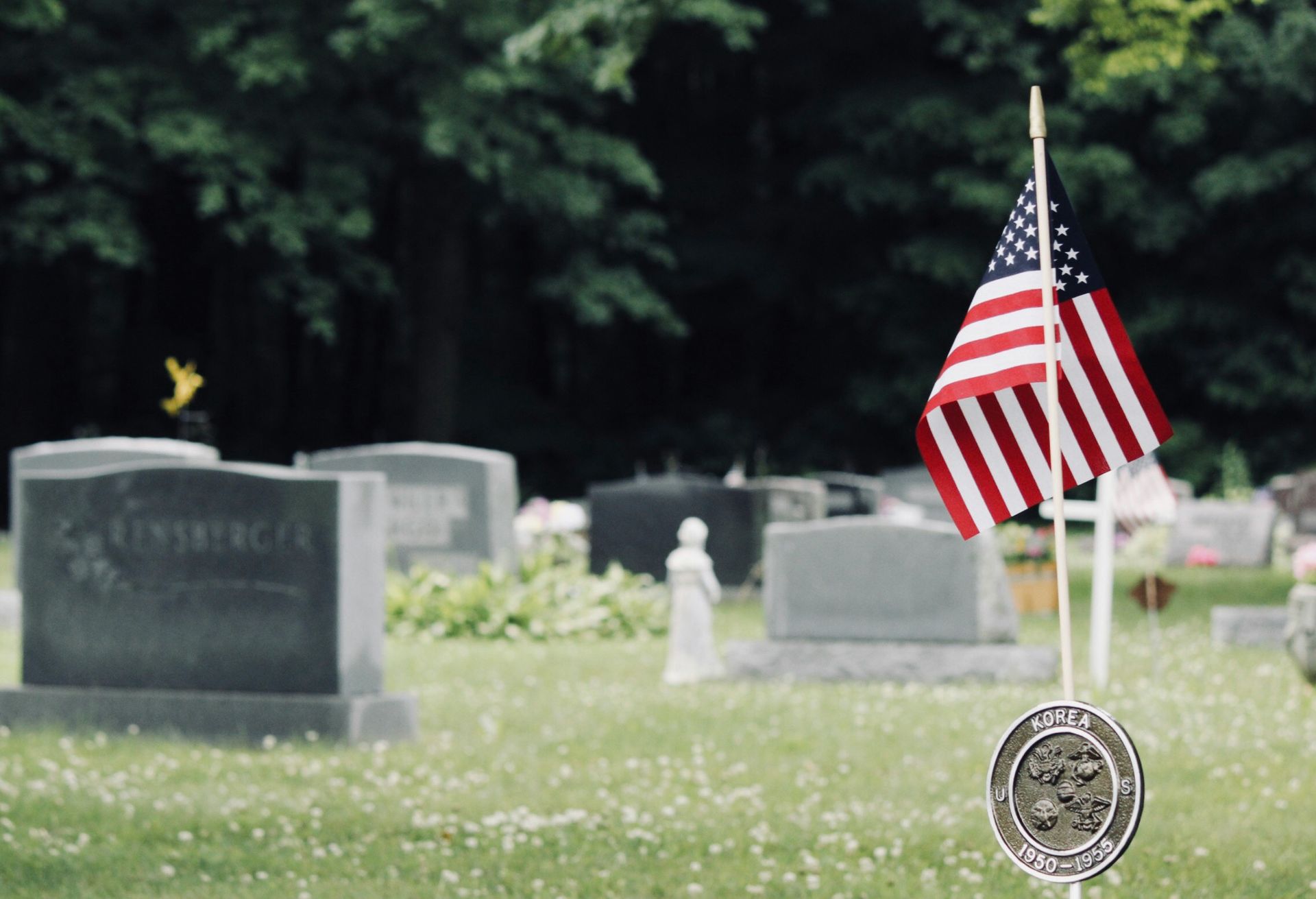 American flag and memorial marker in a cemetery with rows of gravestones and trees