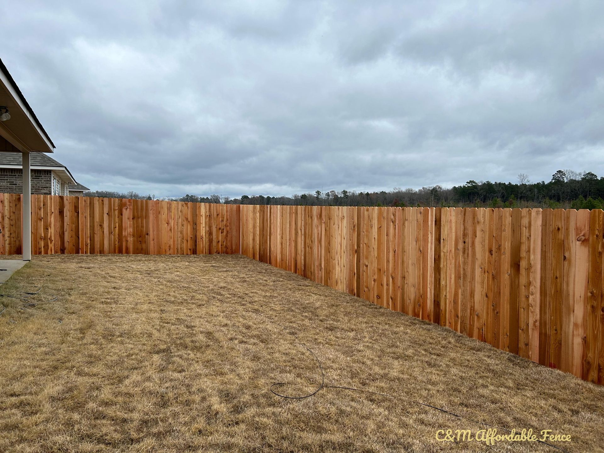 Brown wooden fence encloses a grassy backyard under a cloudy sky.