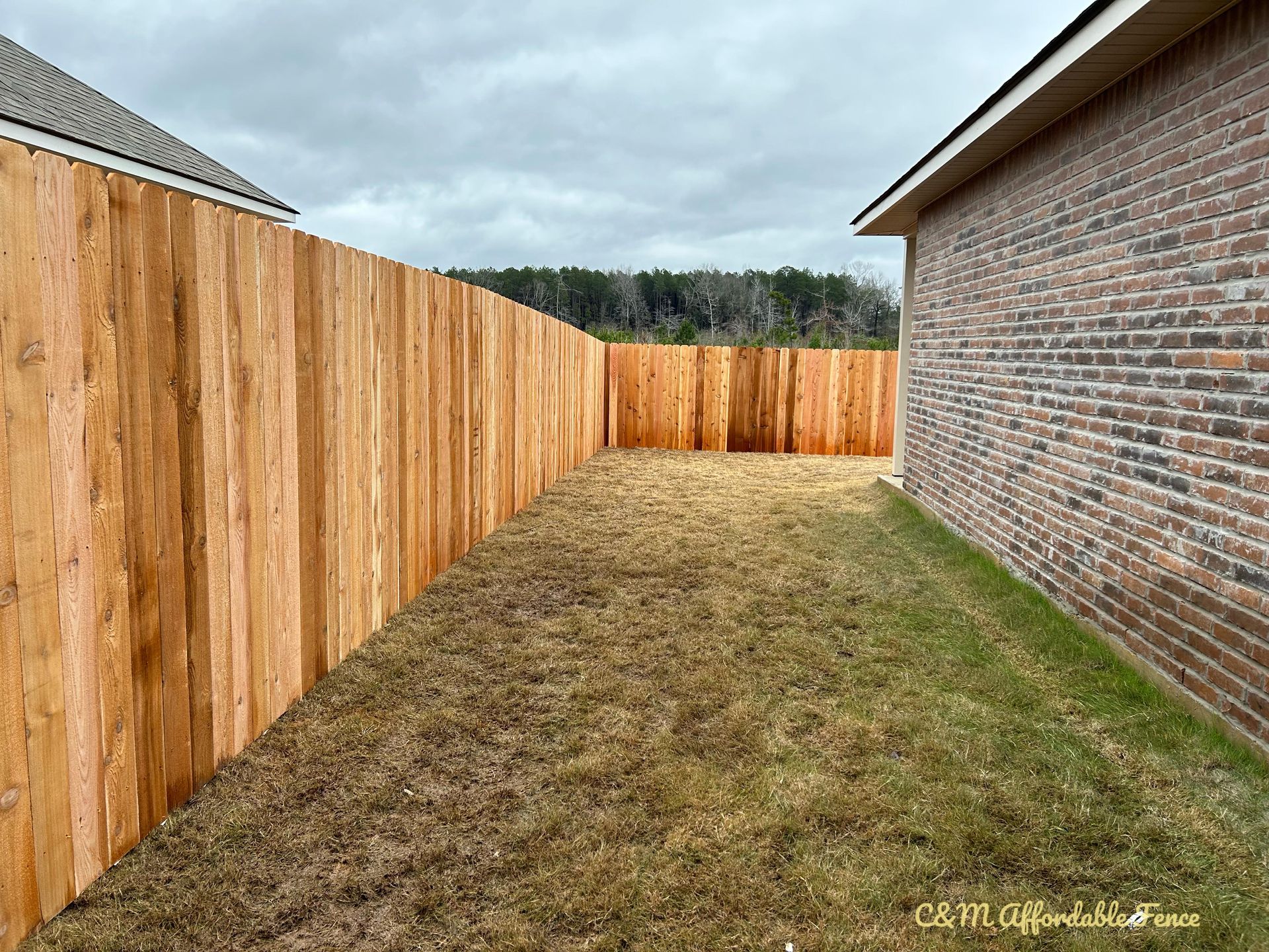A wooden fence is in the backyard of a brick house.