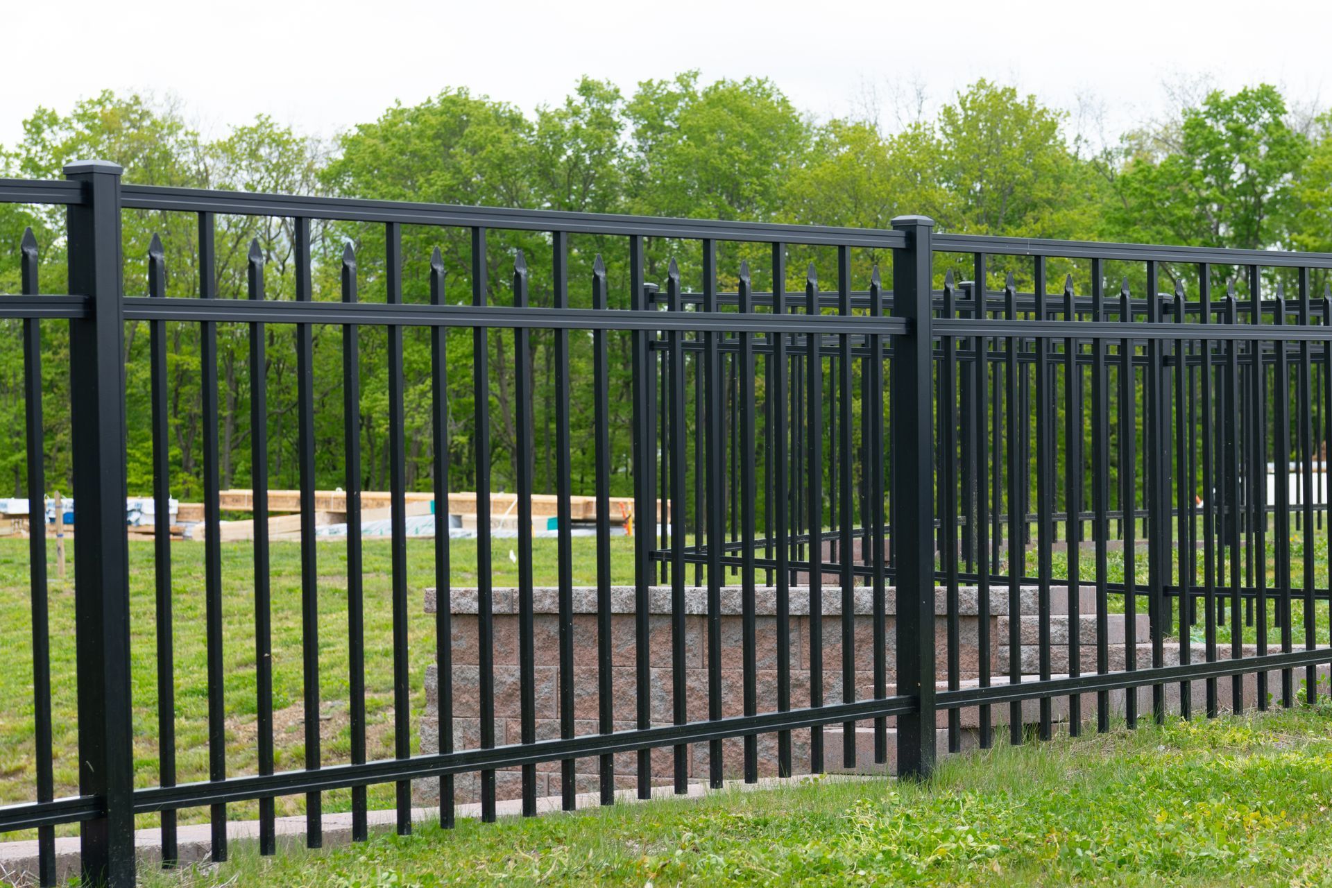 Black metal fence in front of a green grassy area and trees.