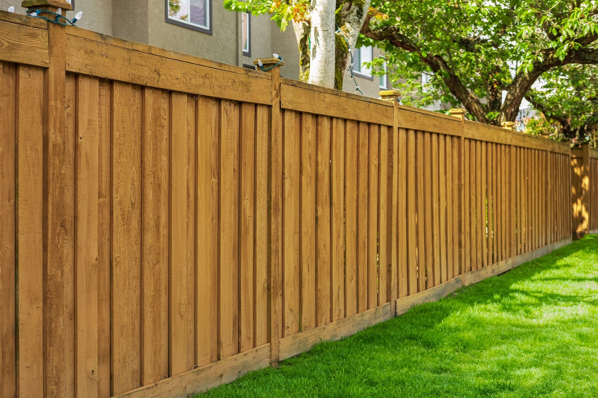 A wooden fence surrounds a lush green lawn in front of a house.