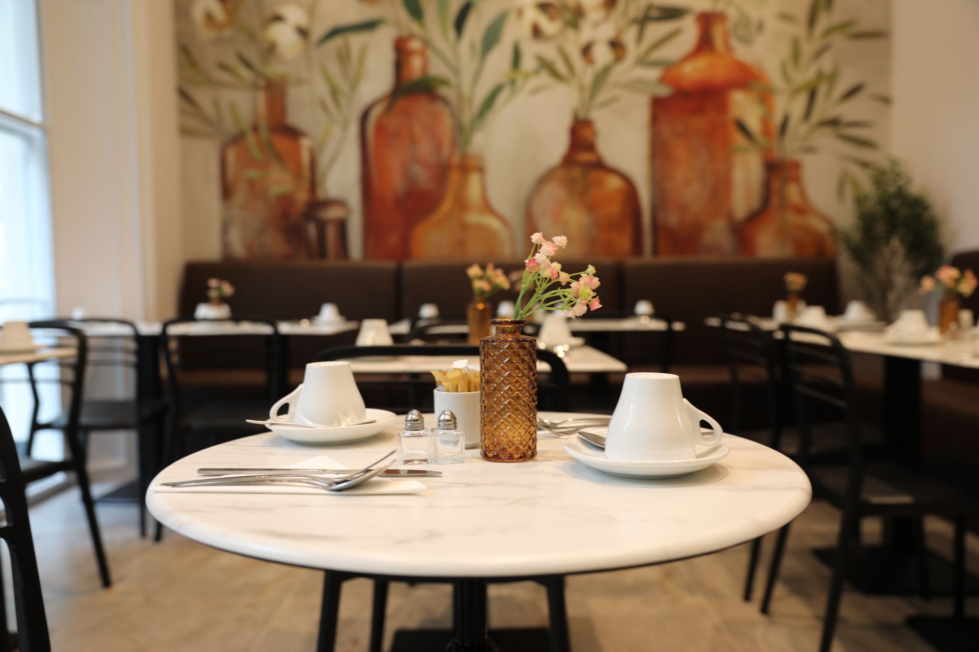 A dining room with tables and chairs and a vase of flowers on the table.