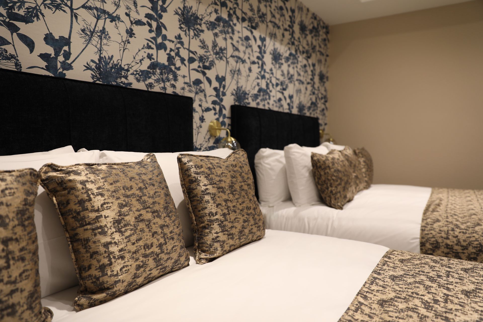 A hotel room with two beds and a floral wallpaper on the wall.