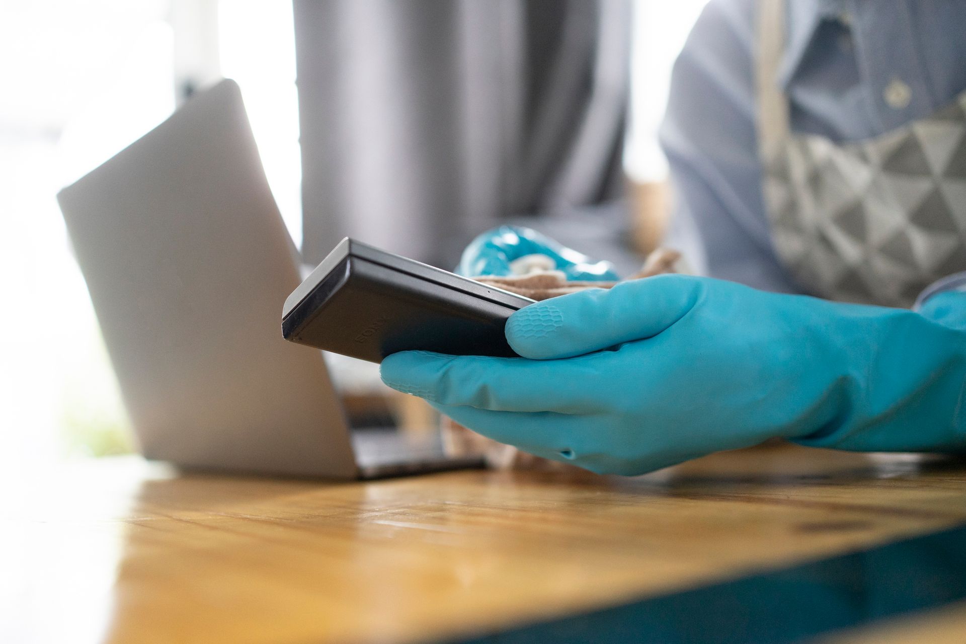 A Person Wearing Blue Gloves Is Holding A Cell Phone In Front Of A Laptop — Cheyenne, WY — Top Mop C.