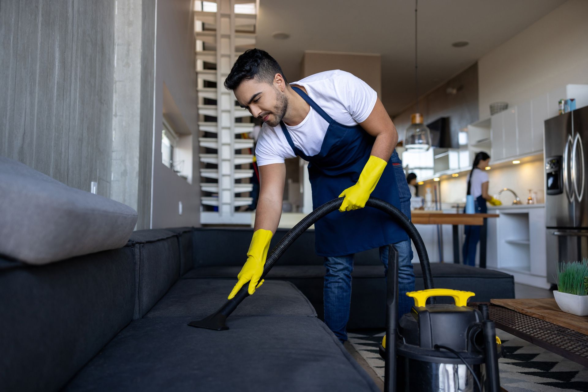 A Man Is Cleaning A Couch With A Vacuum Cleaner In A Living Room — Cheyenne, WY — Top Mop C.