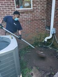 A man is wearing a mask and holding a shovel in front of an air conditioner.