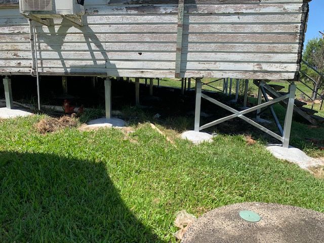 A house on stilts is sitting on top of a lush green field.