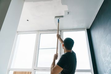 A man is painting the ceiling of a room with a paint roller.