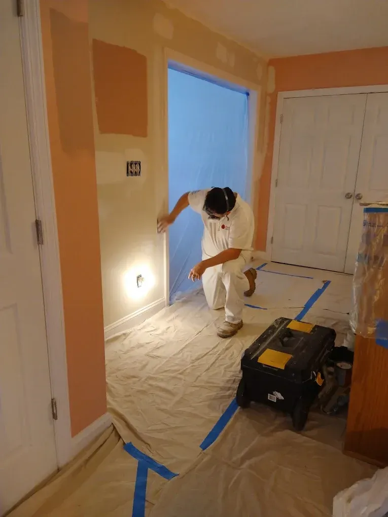 A man is kneeling down in a room painting a wall.