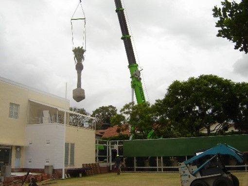 A green crane is lifting a large object in front of a building