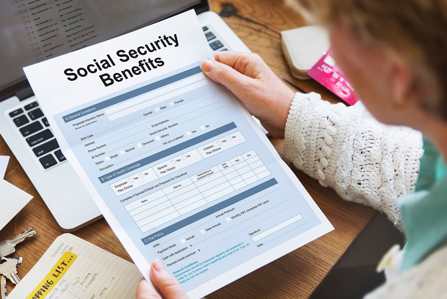 Person reviewing a Social Security benefits form at a desk with a laptop.
