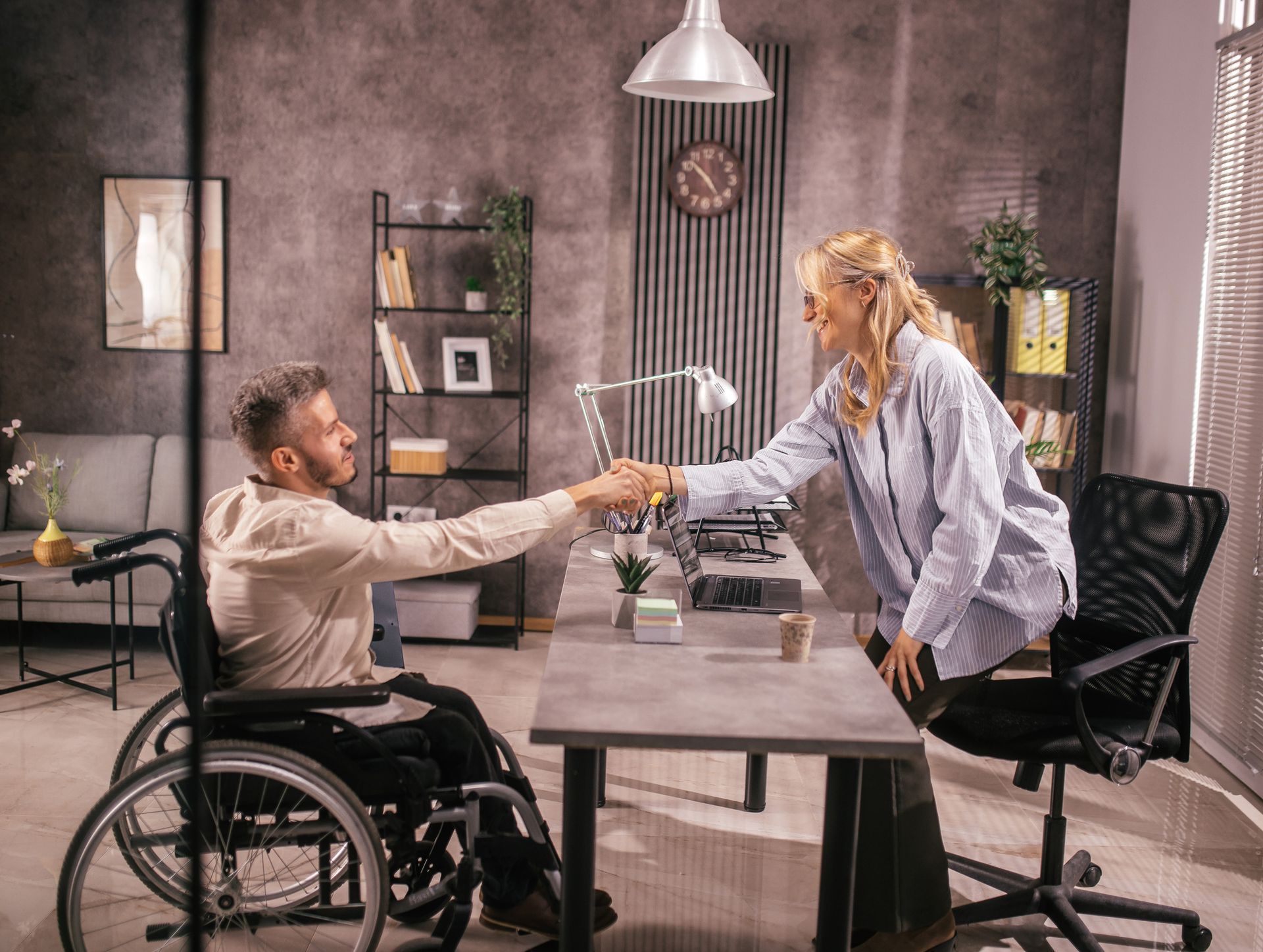 A young man in a wheelchair shaking hands with his social security disability attorney in her office. A young man in a wheelchair shaking hands with his social security disability attorney in her office.