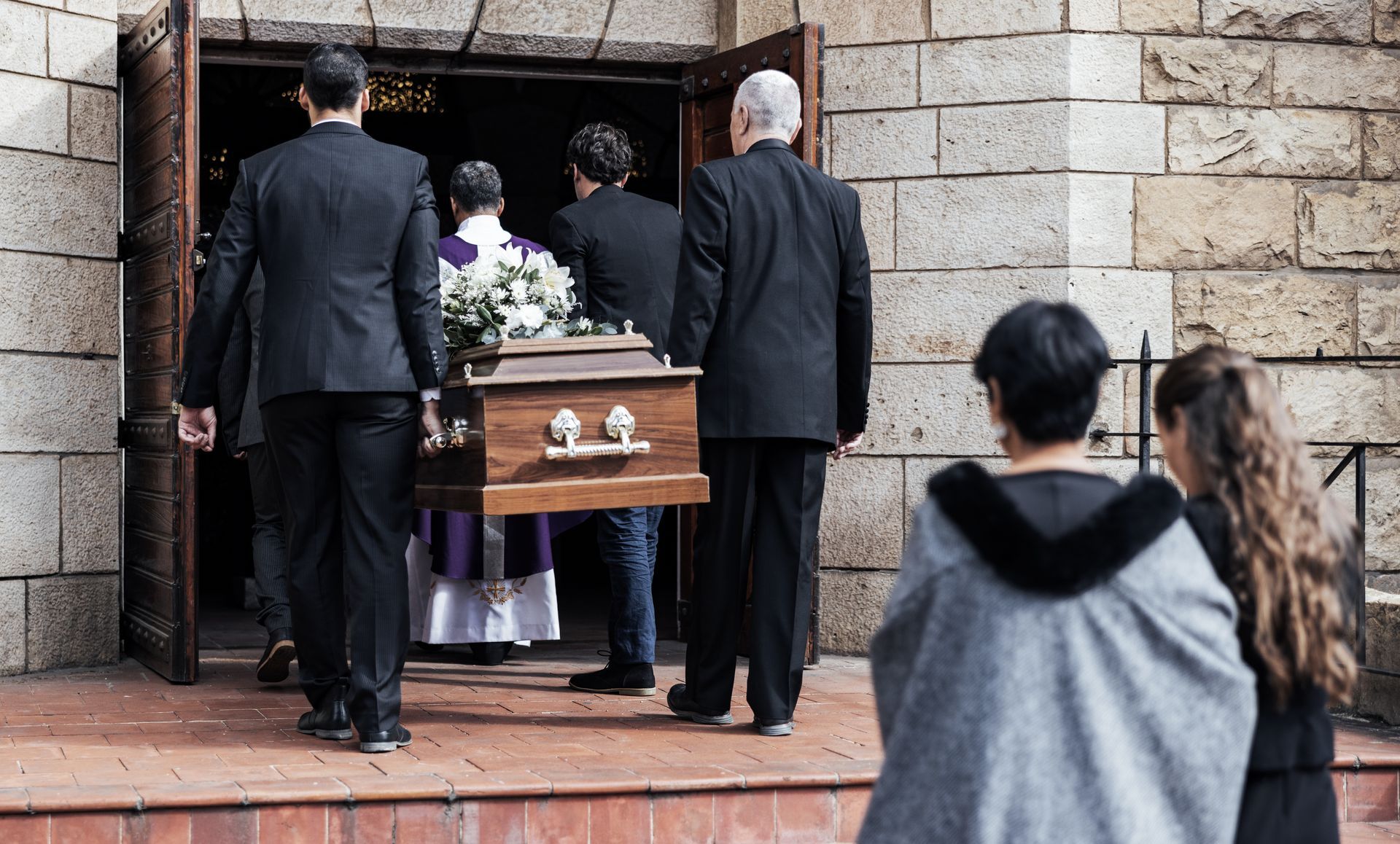 Mourners carrying a flower-decked coffin into a stone chapel entrance