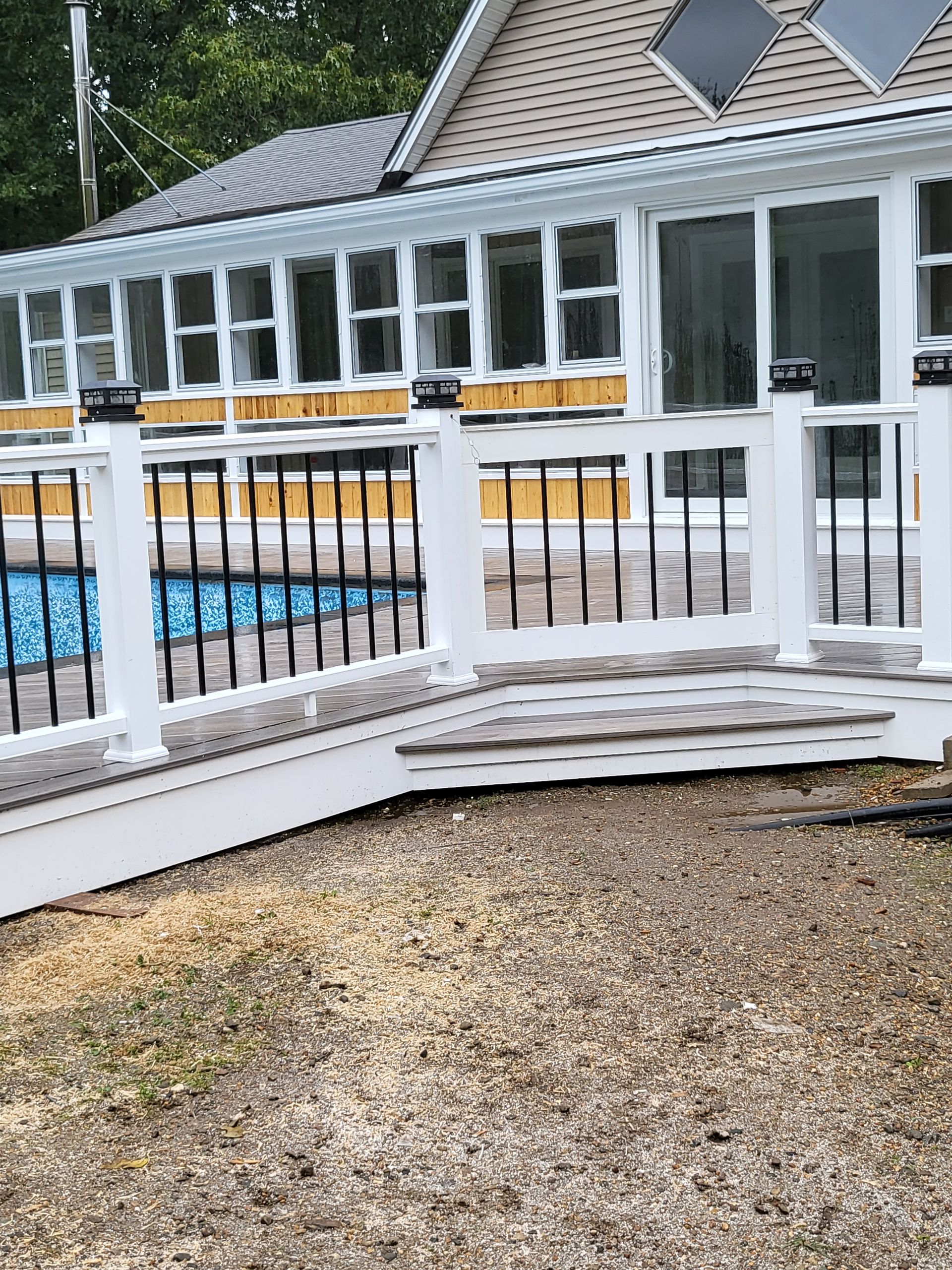 A white fence surrounds a house with a pool in the background.
