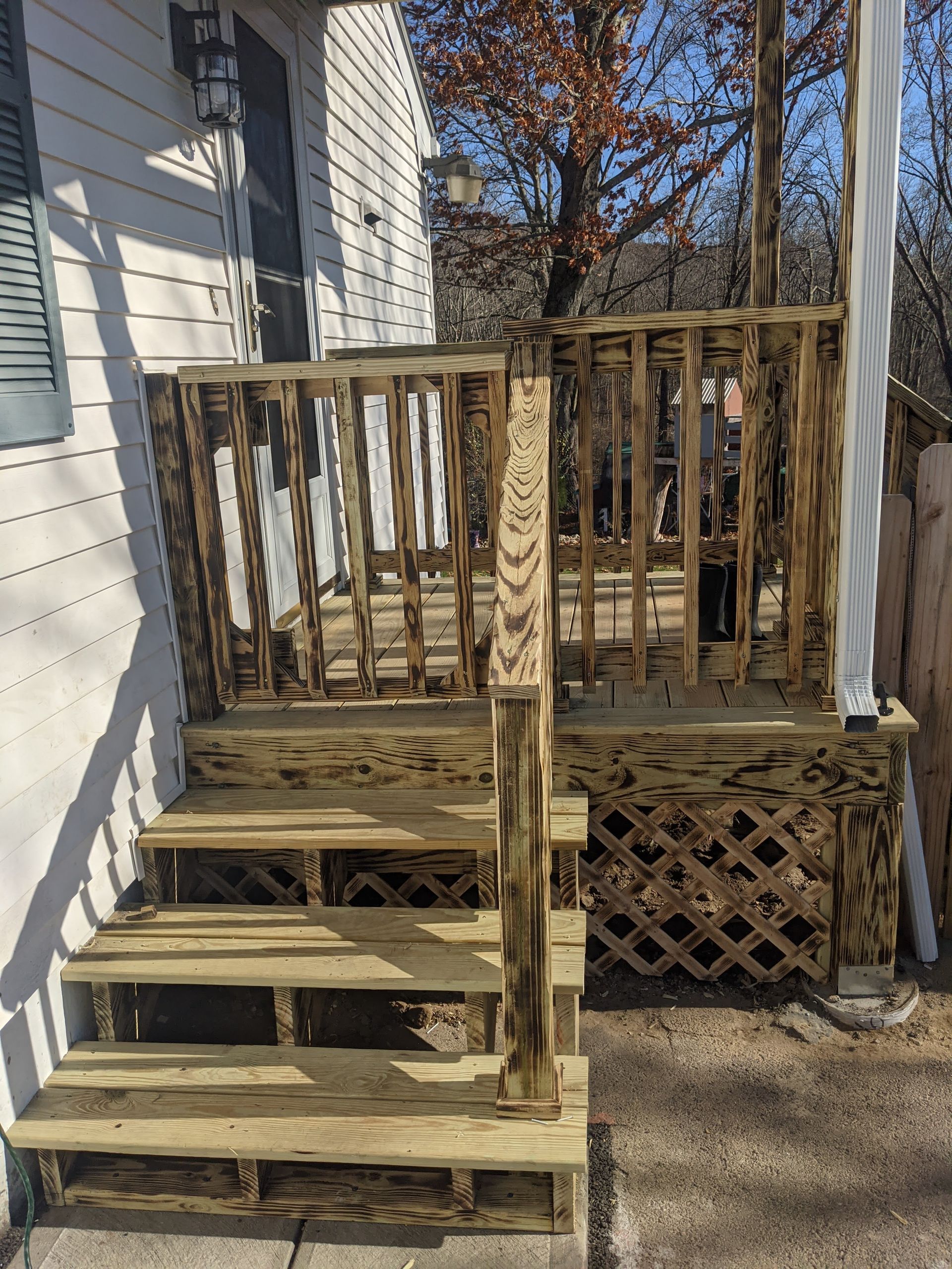 A wooden deck with stairs leading up to it is in front of a white house.