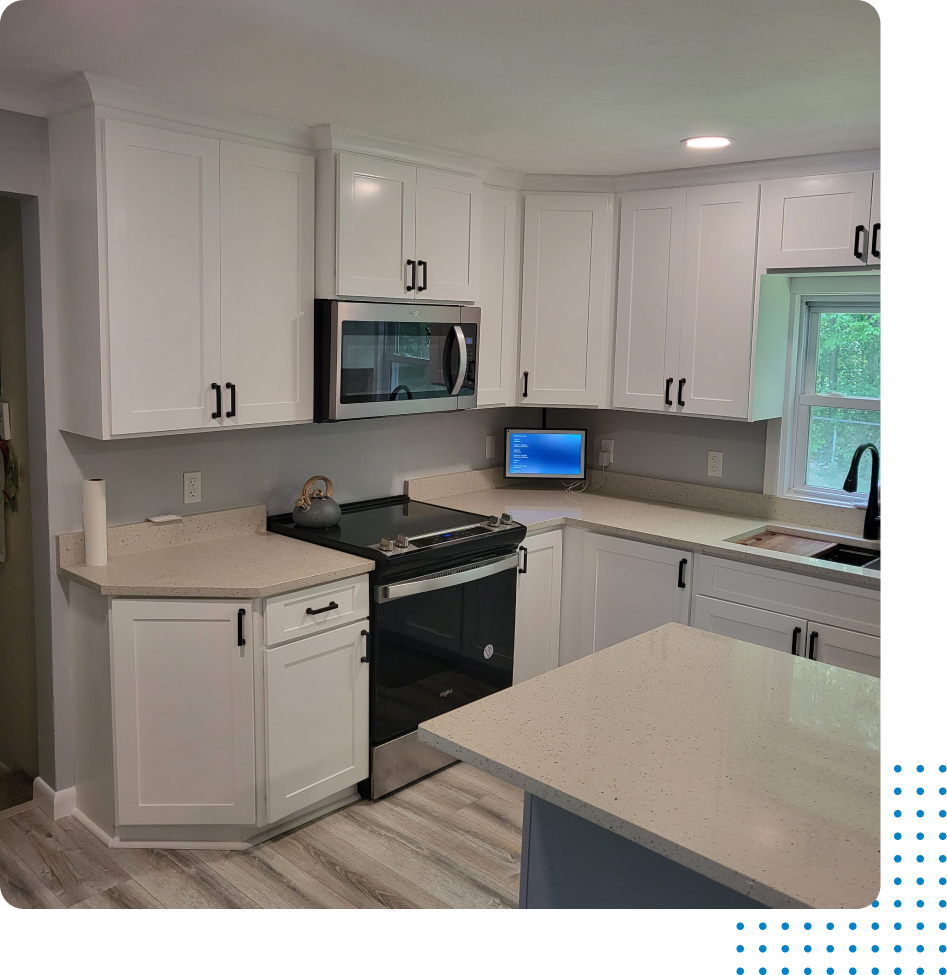 A kitchen with white cabinets , a stove , a microwave , and a laptop on the counter.