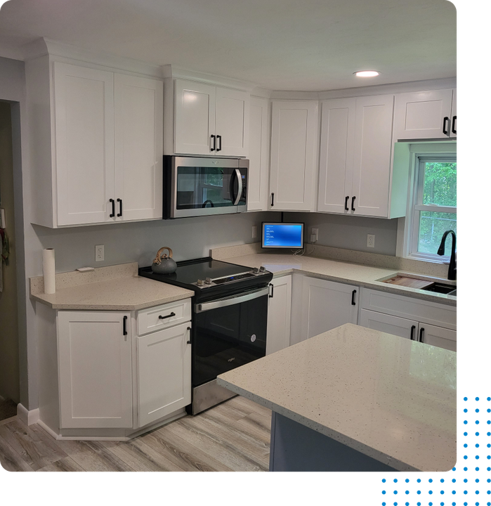 A kitchen with white cabinets , a stove , a microwave , and a laptop on the counter.