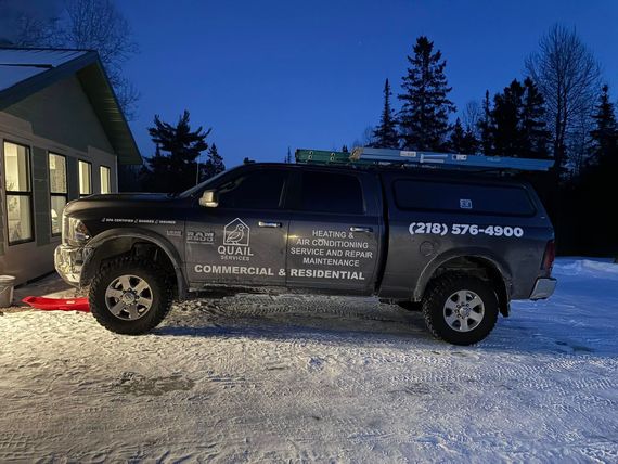 Black commercial SUV parked in snowy driveway beside a lit house at dusk, with service logos on the side
