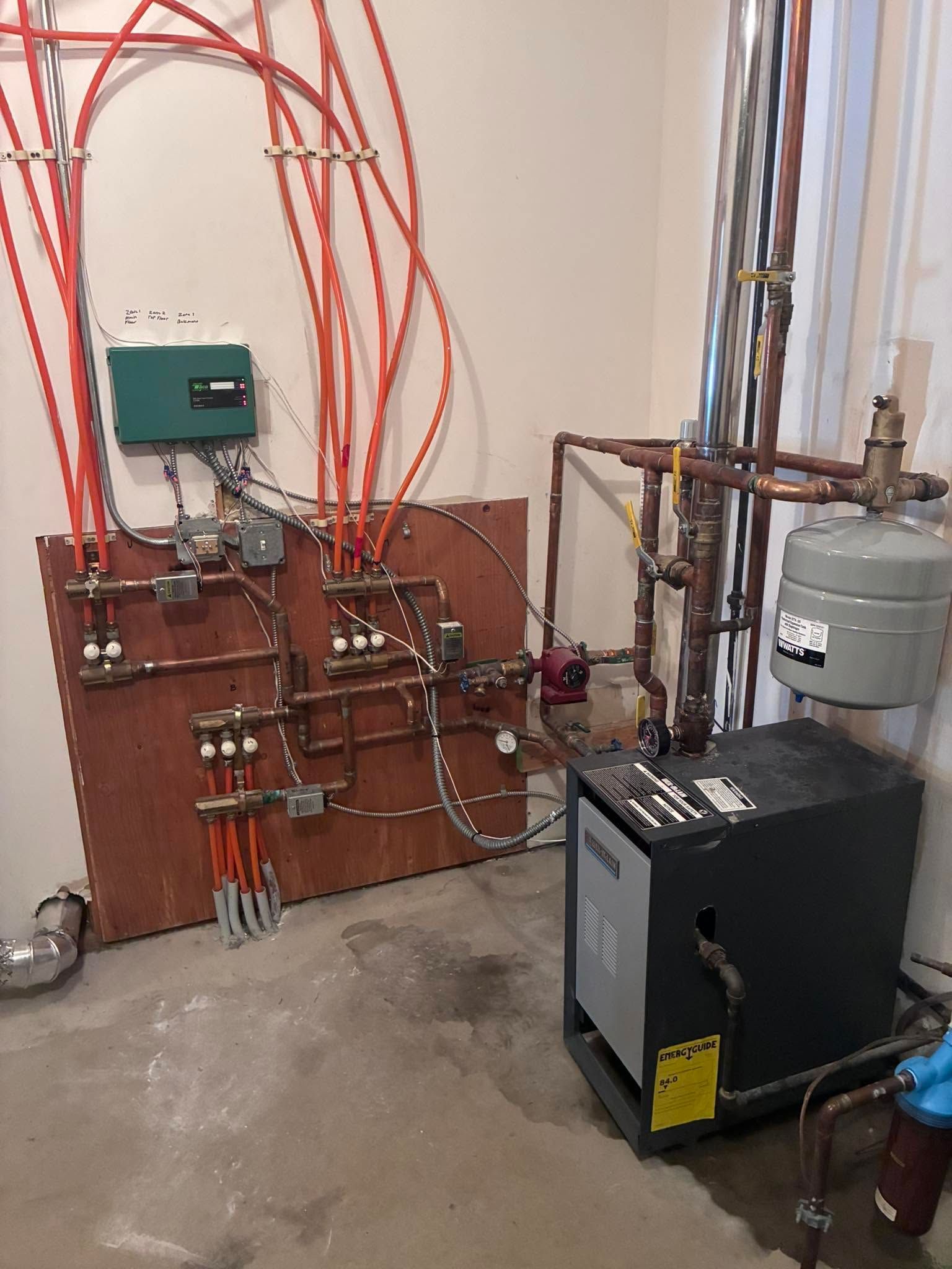 Boiler room with pumps, tanks, and red pipes mounted on a concrete wall and floor.