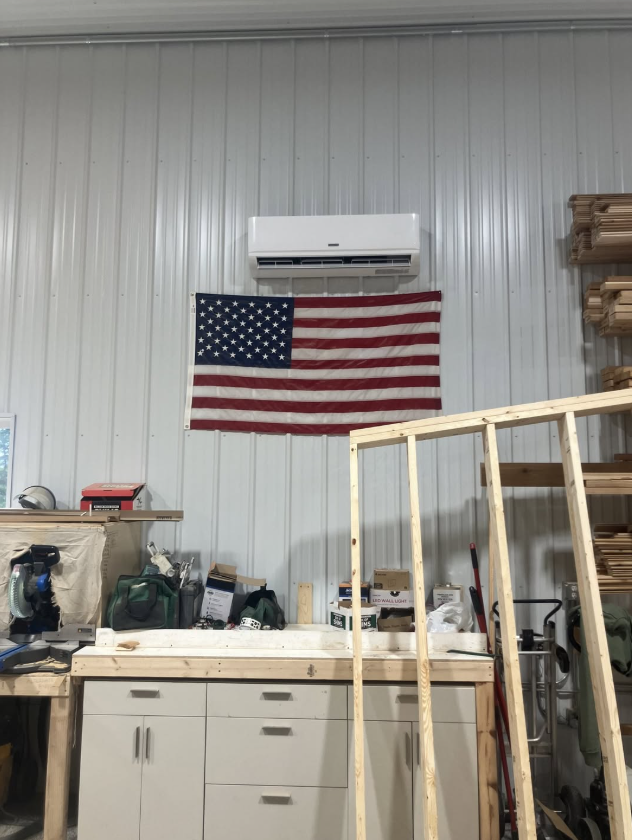 Workshop wall with an American flag under a wall-mounted air conditioner, above a workbench.