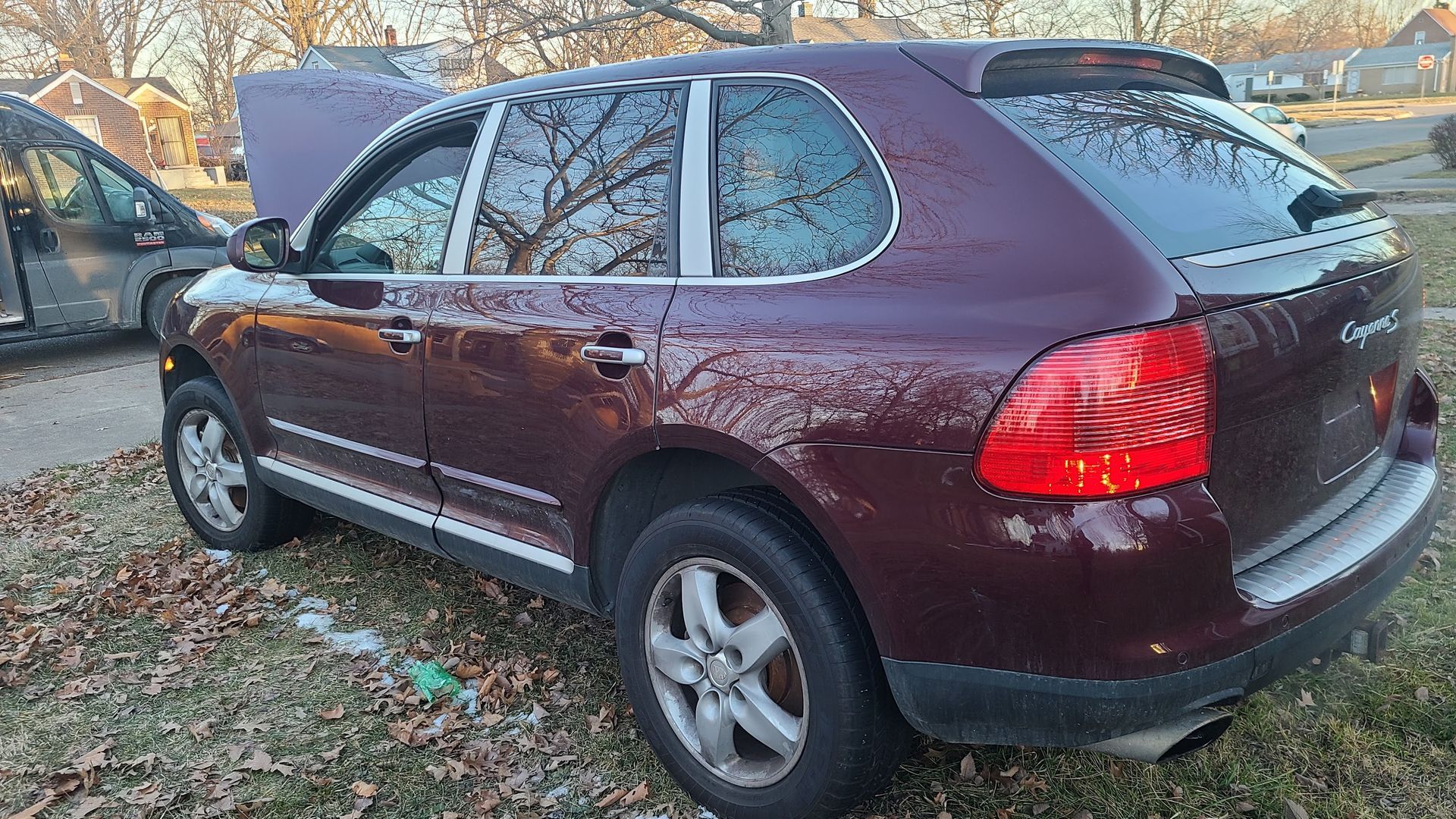 Maroon Porsche Cayenne SUV with the hood open, parked on grass.