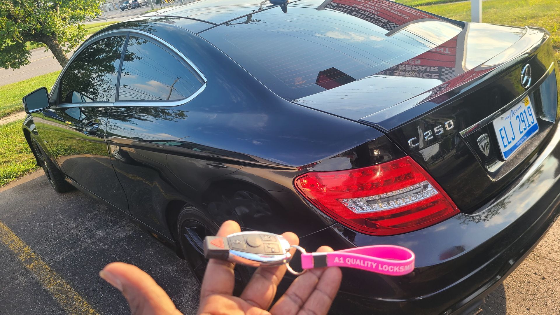 Hand holding car key with pink fob, black Mercedes-Benz coupe in the background.