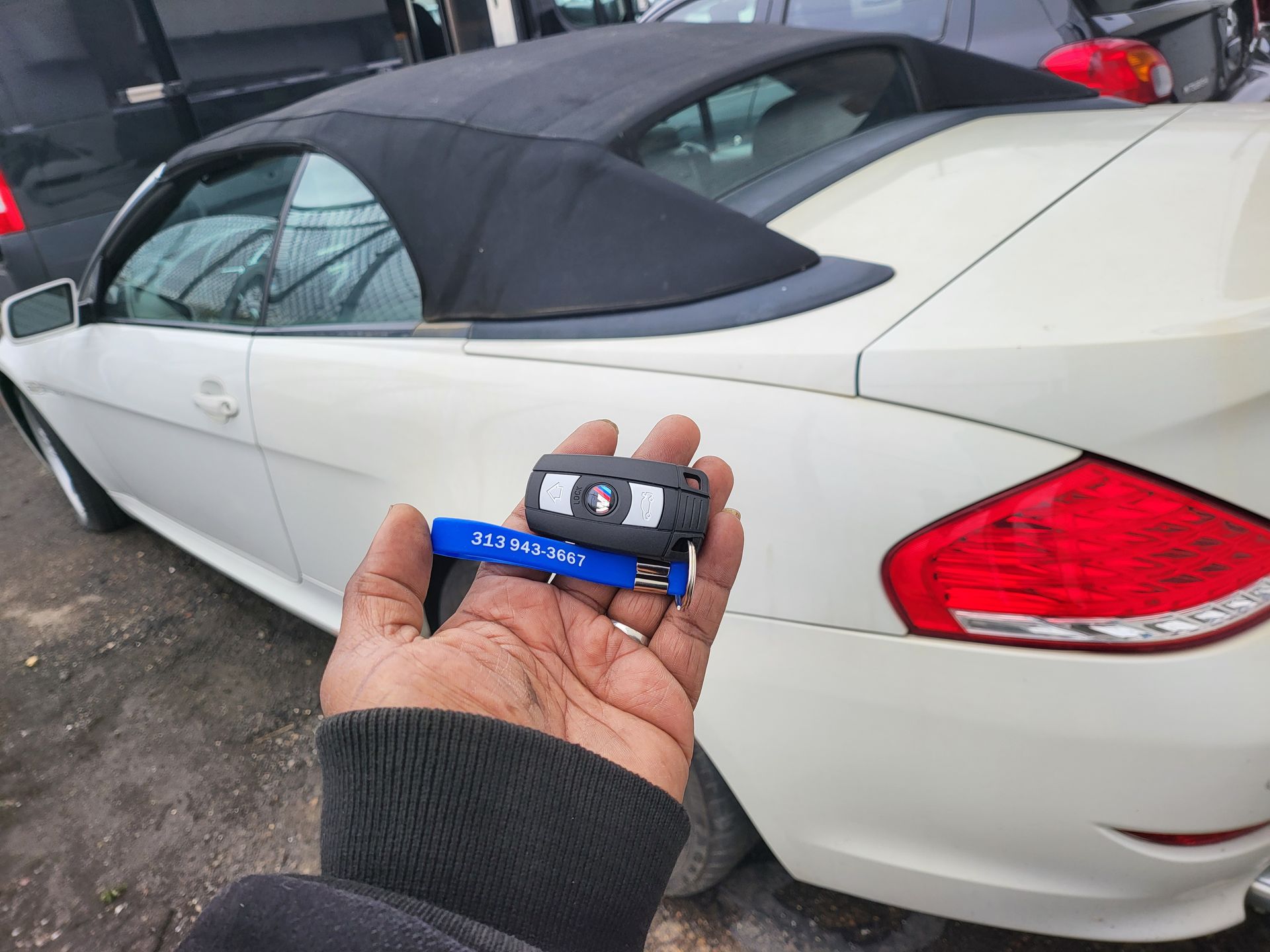 Hand holding car keys in front of a white BMW convertible.