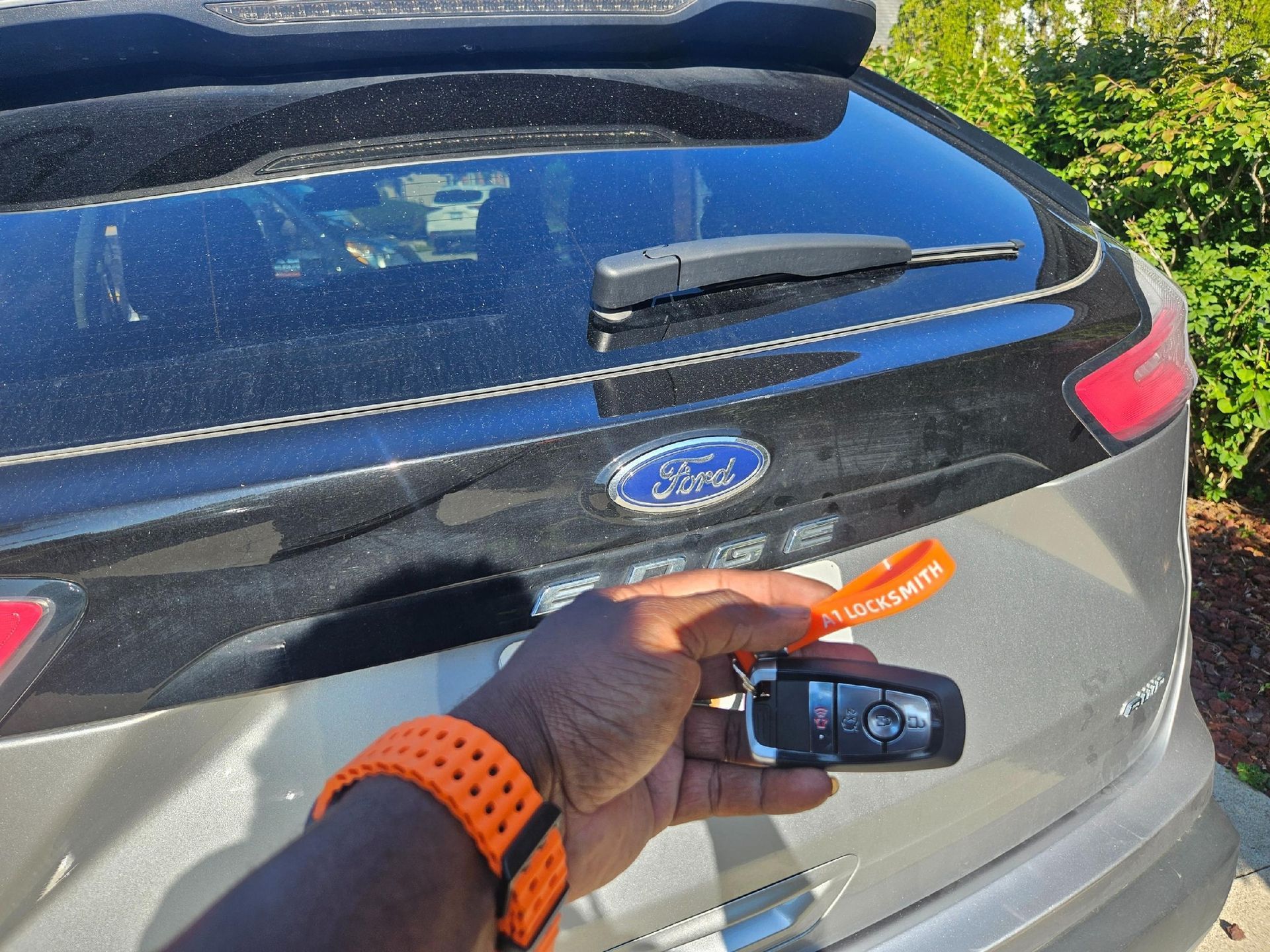 Person's hand holding a car key near the rear of a Ford SUV. Key has an orange lanyard.