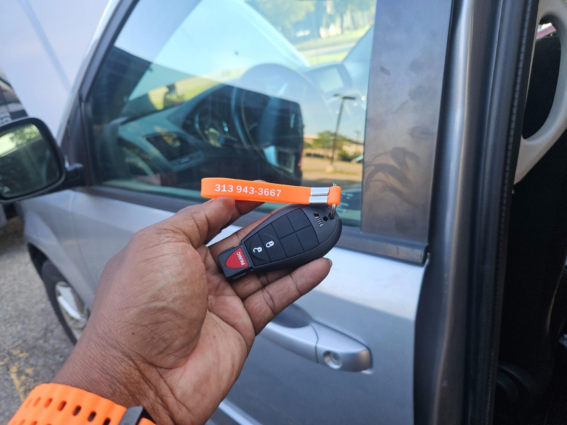 Hand holding car key and a small orange tool next to a silver car door.
