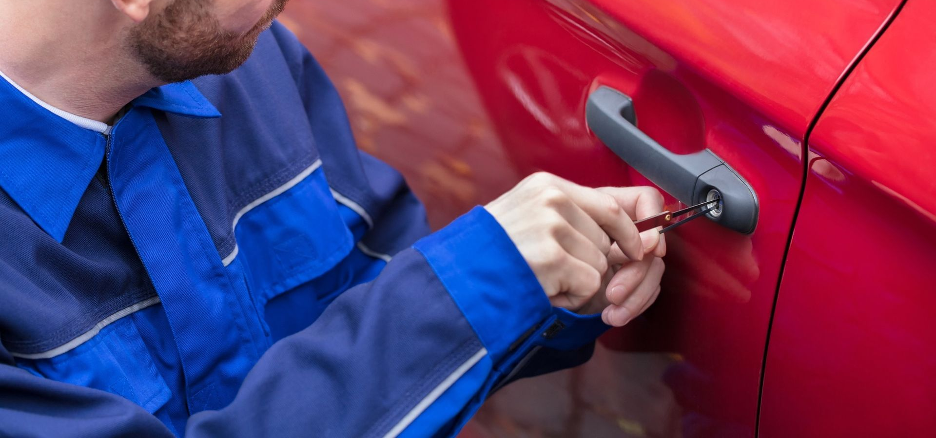 Person unlocking a red car door with a key; they wear a blue jumpsuit.