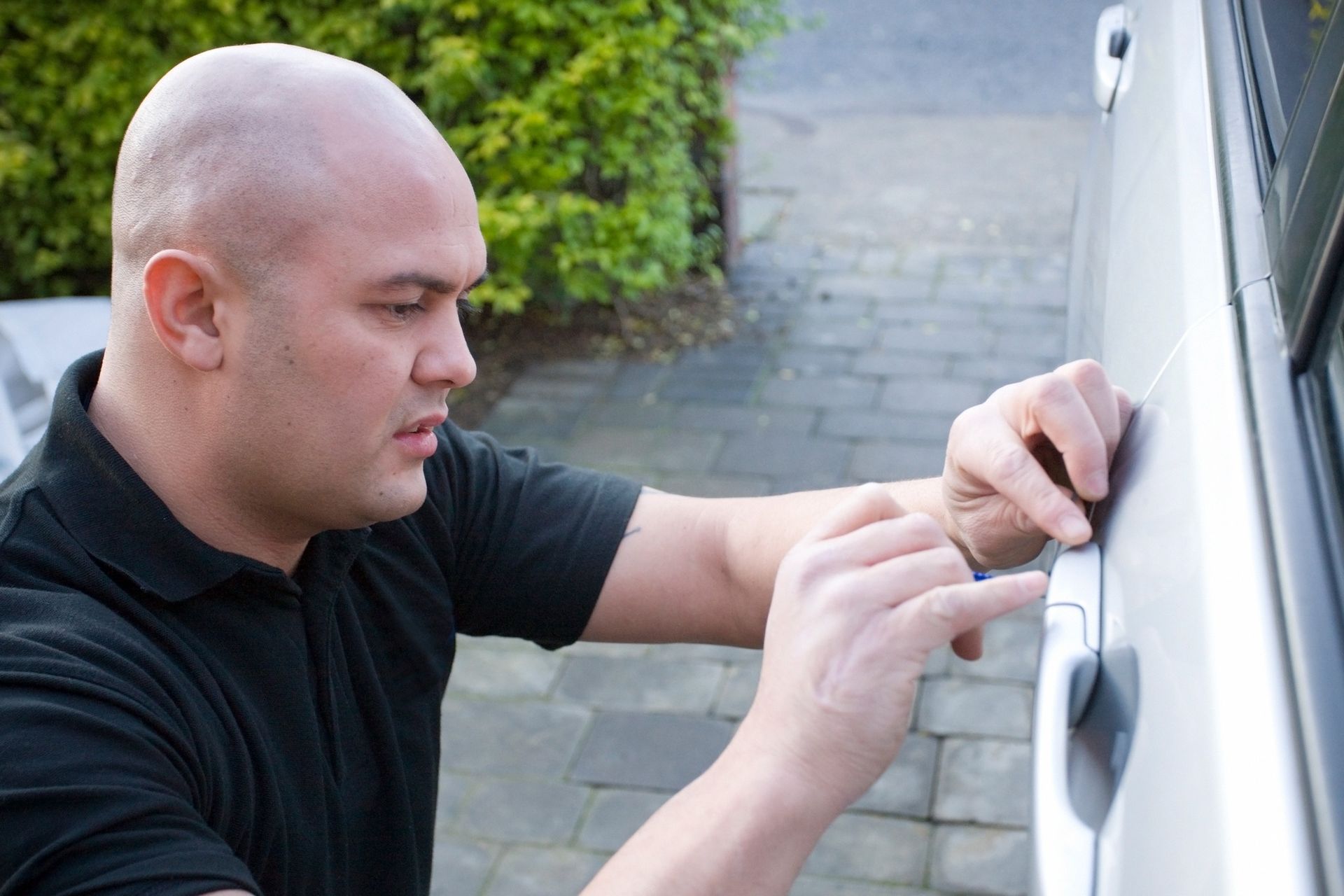 Man with bald head intently trying to unlock car door.