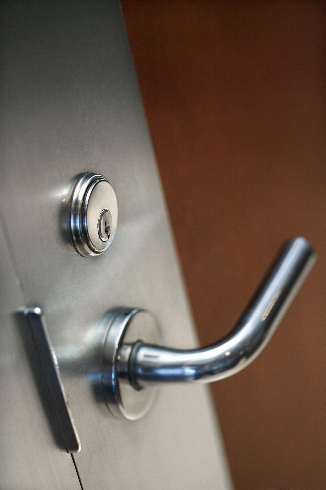 Silver door with a lock, handle, and a lock pick in the process of being used. Brown background.