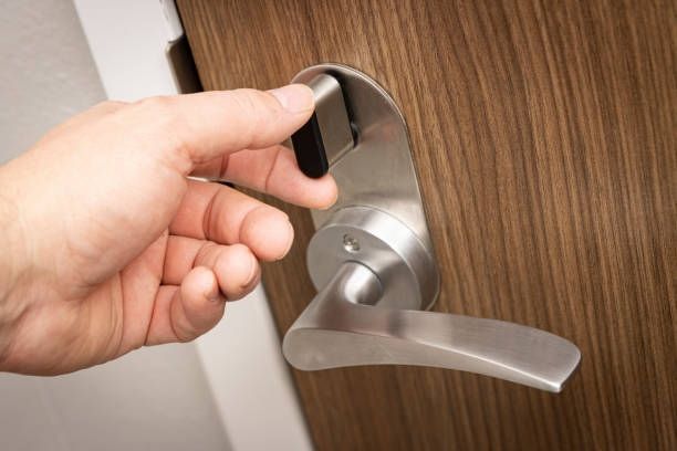 Hand opening a hotel door with a silver handle and a black security slider on a wooden door.