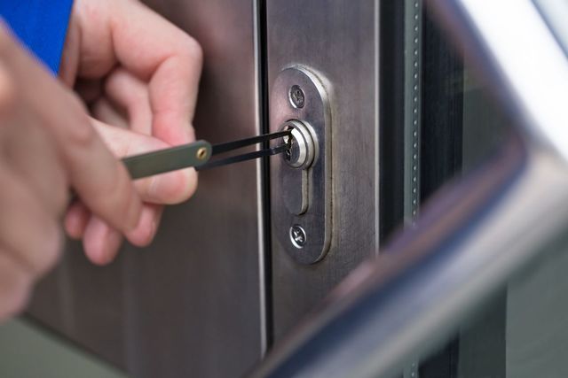 Hands using lock picks to open a metal door's lock.