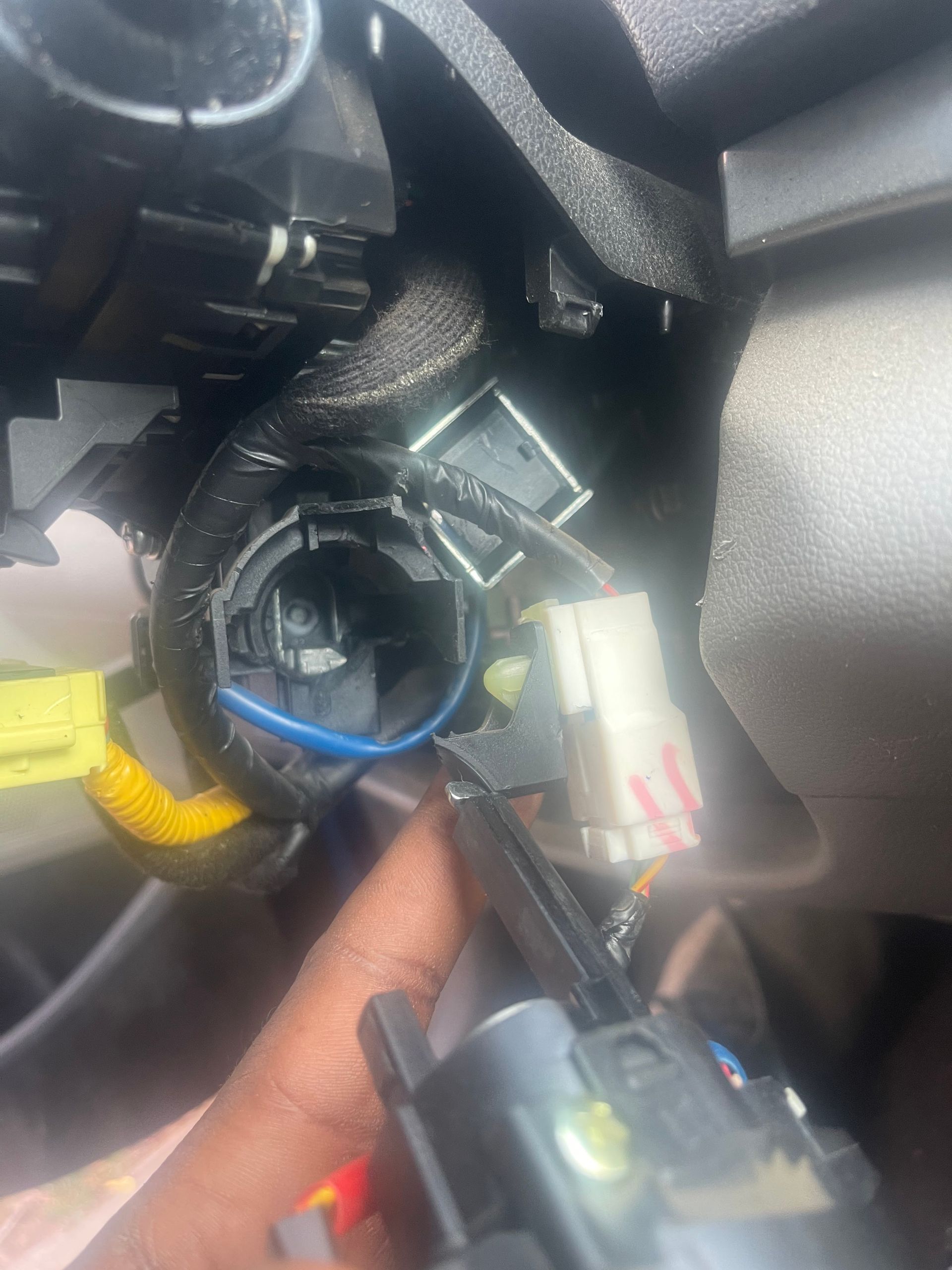 A hand holding a screwdriver near a car ignition switch with exposed wires and connectors.