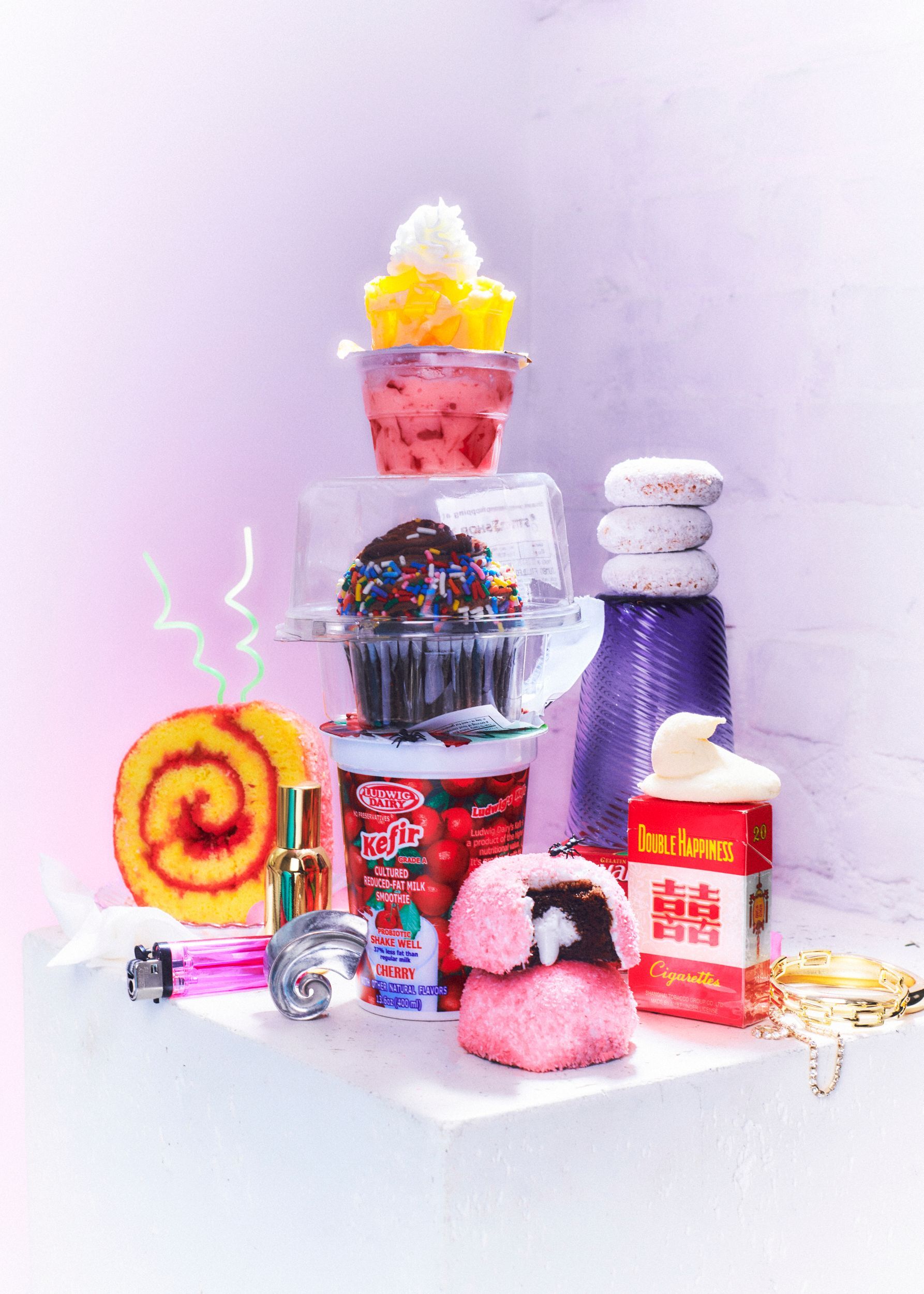 Pink frosted treats, cupcakes, and a bottle in a still life against a pastel background. Food Stylist Nadine Page.