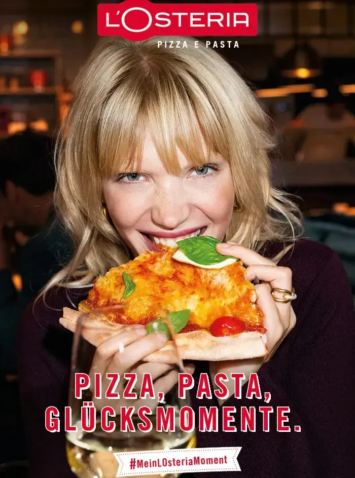 Woman eating pizza, holding wine, smiling. L'Osteria restaurant ad. Food Stylist Nadine Page.