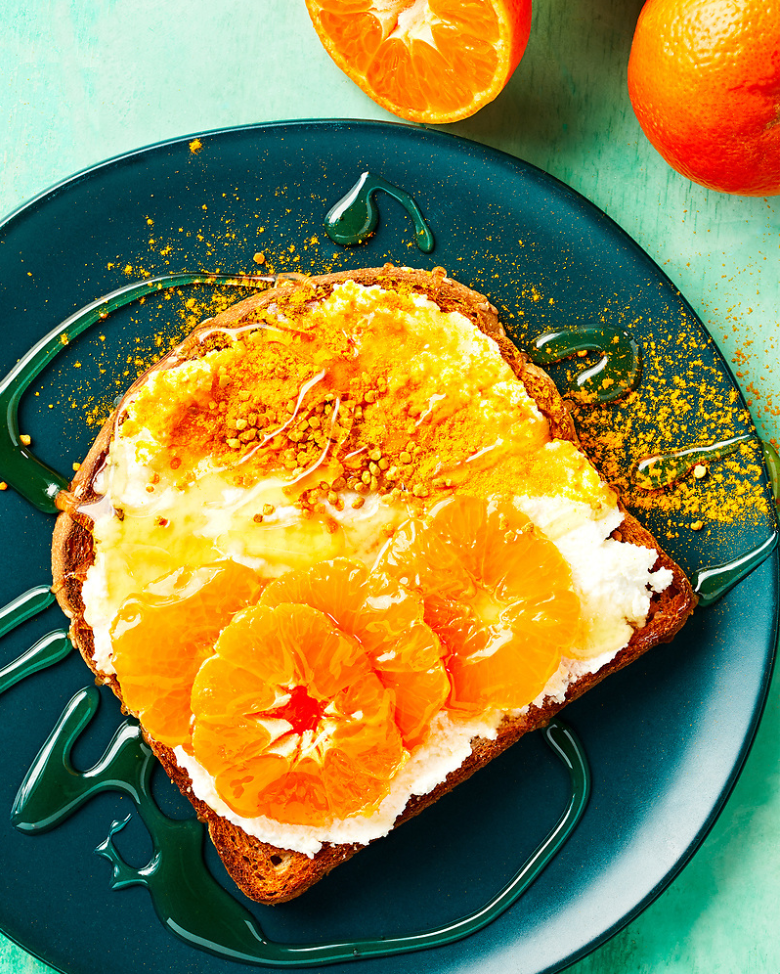 Toast topped with cream cheese, orange slices, and honey on a teal plate; oranges in background. Food Stylist Nadine Page.