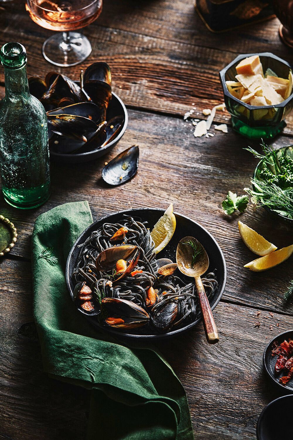 Black pasta with mussels on a rustic wooden table, garnished with lemon and herbs. Food Stylist Nadine Page.