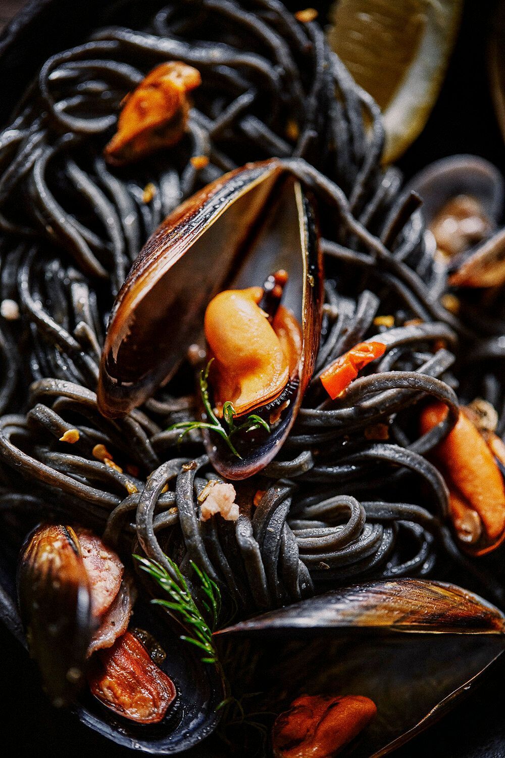Black squid ink pasta with mussels. Close up shot with dark colors and herbs. Food Stylist Nadine Page.
