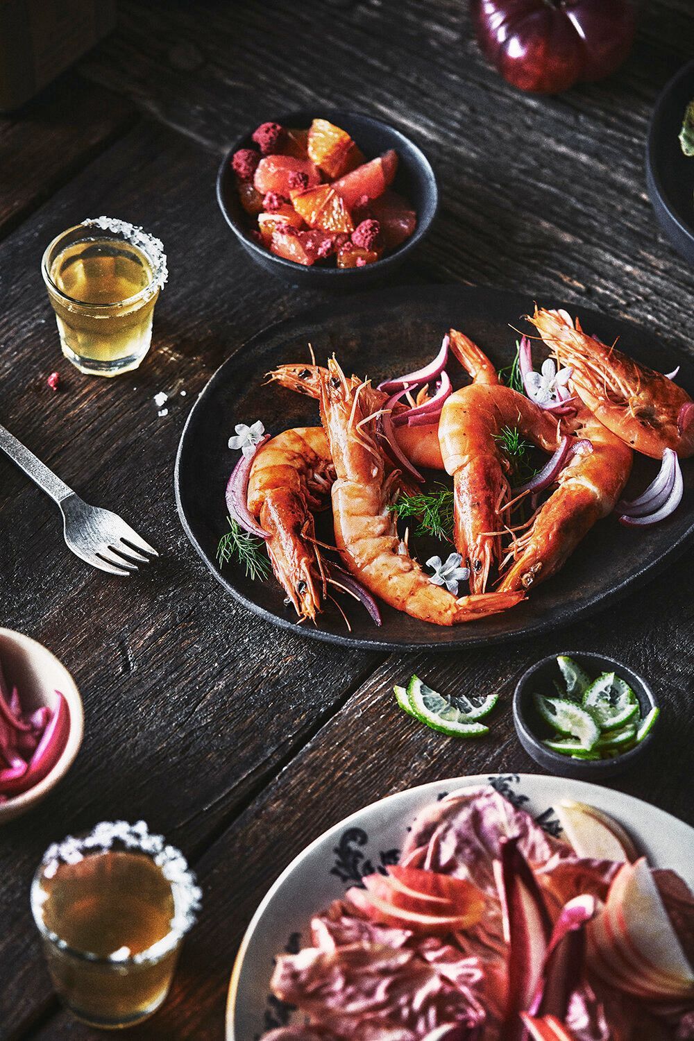 Grilled shrimp dish with red onions, lime, and tequila shots on a rustic wooden table. Food Stylist Nadine Page.