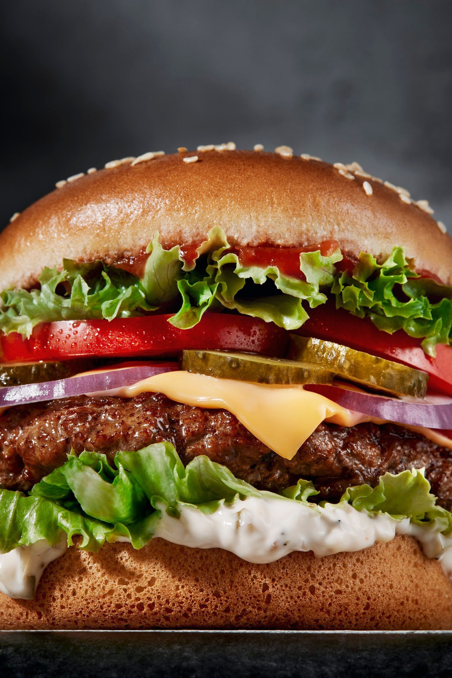 A close-up of a hamburger with sesame seed bun, lettuce, tomato, pickles, onion, cheese, and sauce. Food Stylist Nadine Page.