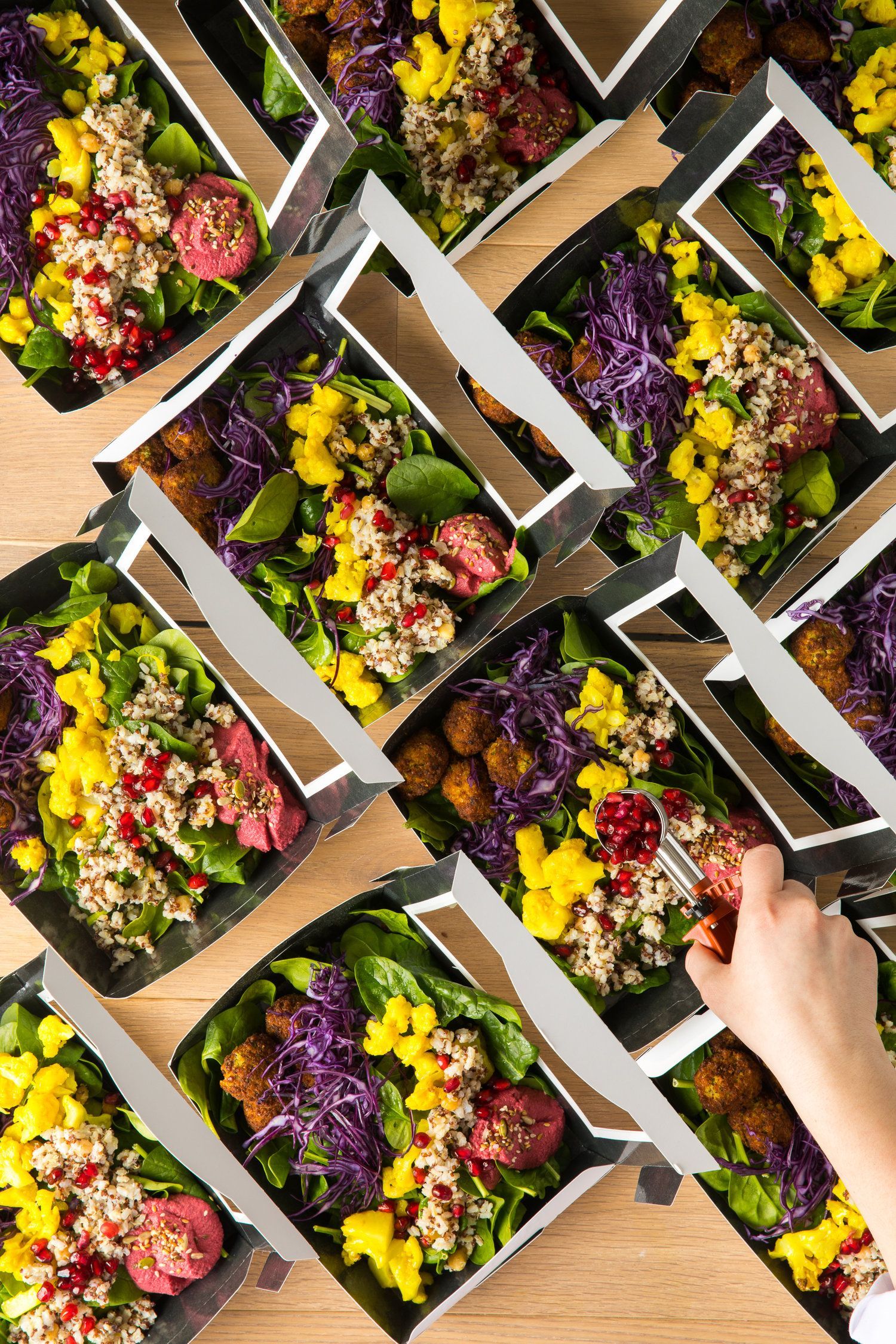 Overhead shot of several pre-packaged salads in black boxes, with a hand reaching for one. Food Stylist Nadine Page.
