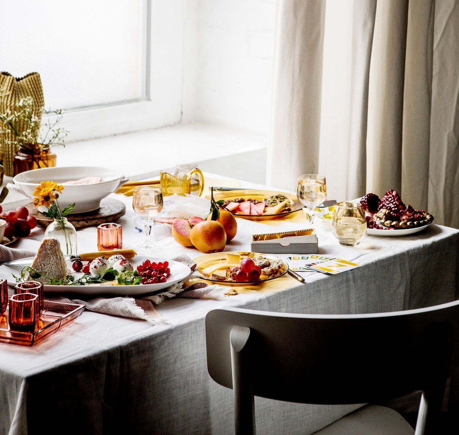 A table set with food, drinks, and flowers near a window.Food Stylist Nadine Page.