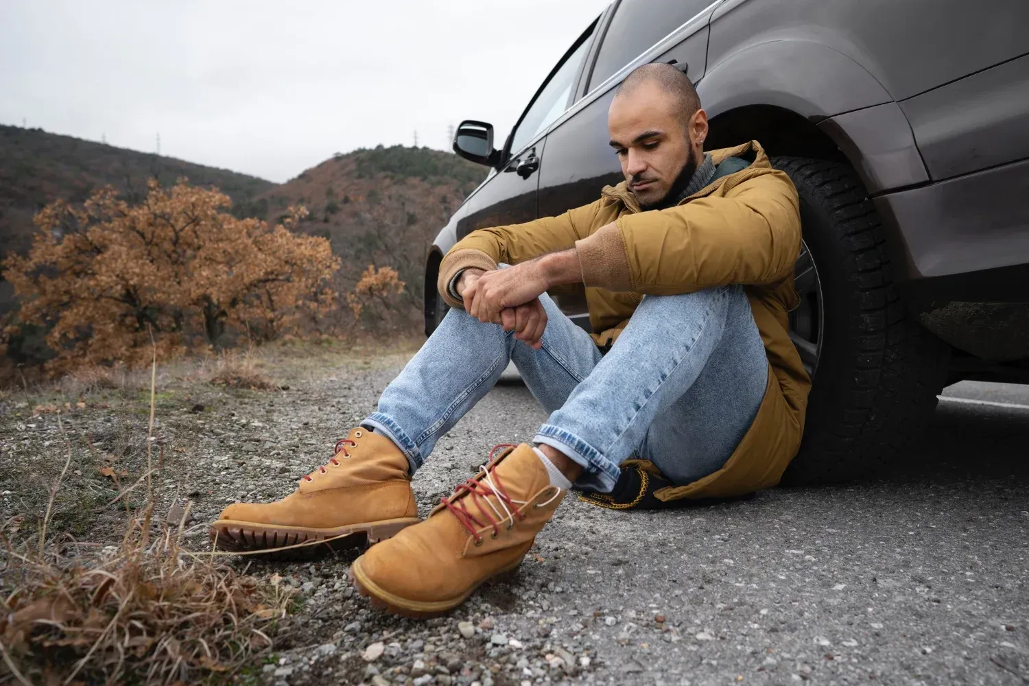 pensive man leans againt the wheel of his car at the side of the road