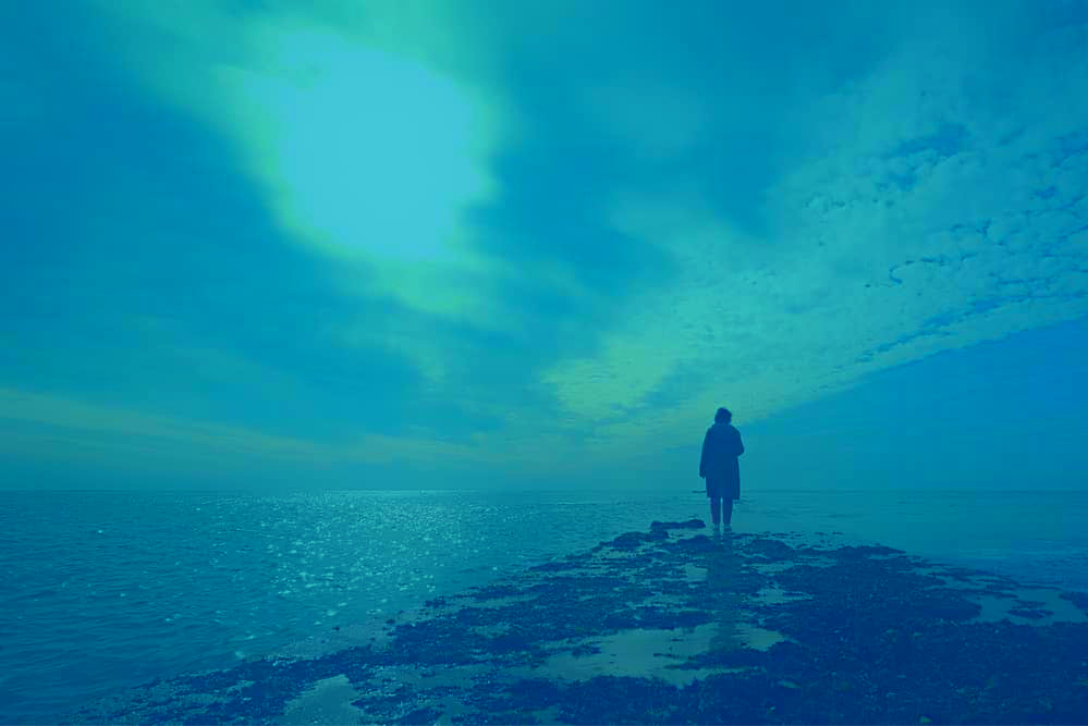 Person sanding at the edge of a rocky beach, looking at the horizon
