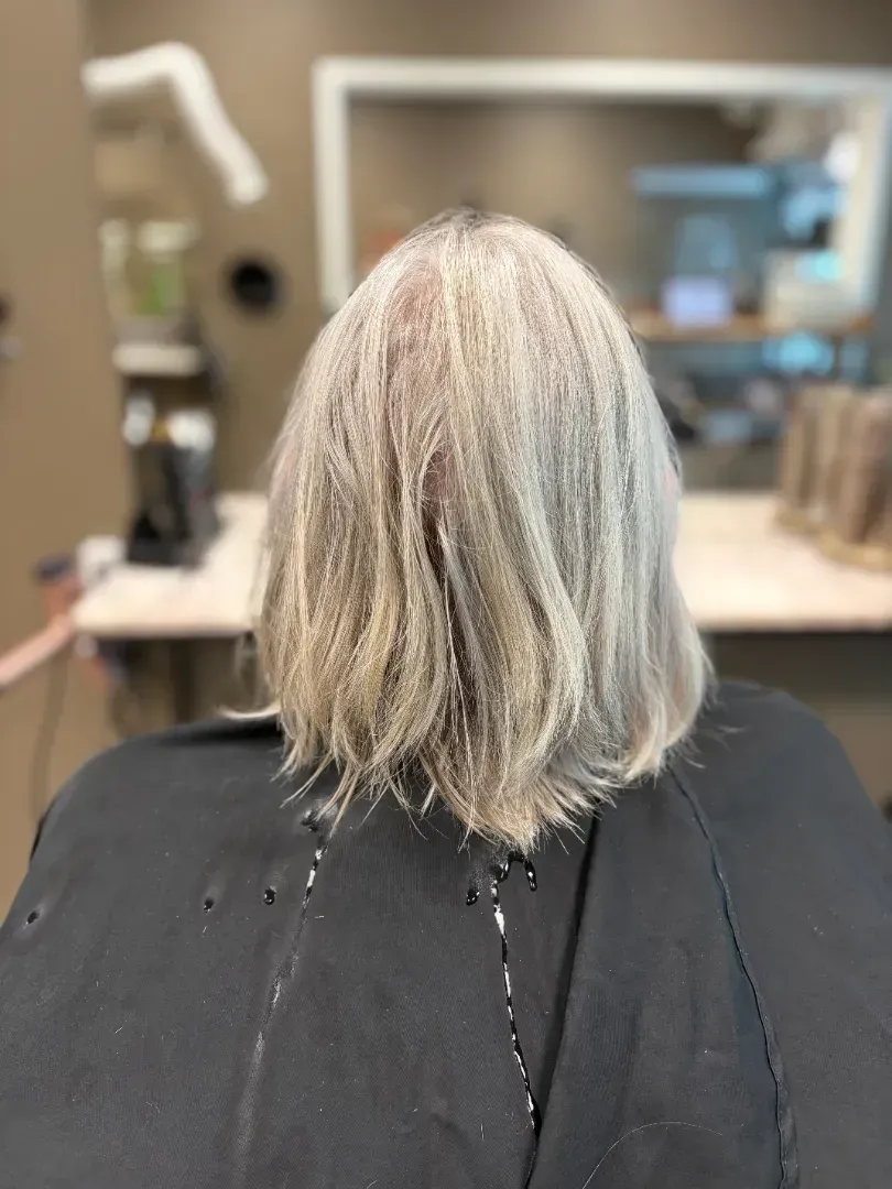 Person with gray, shoulder-length hair at a salon, wearing a black cape.
